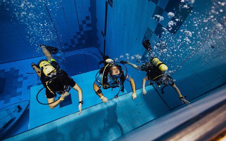 Trzech mężczyzn w pełnym wyposażeniu nurkujący w niebieskim basenie