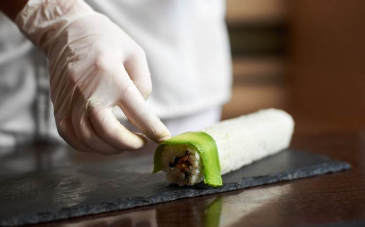 Sushi Master układający cieniutkie plasterki awokado na gotowej długiej rolce sushi