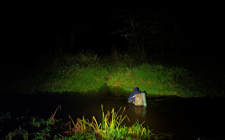 Osoba z pełnym wyposażeniem do biwakowania przechodząca nocą przez rzekę