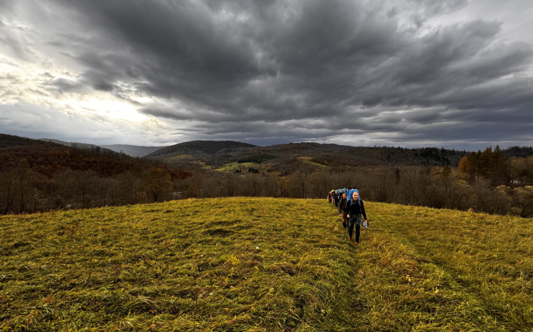 Grupa osób idąca gęsiego przez zielona wzgórza
