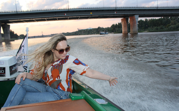 Kobieta siedząca w łódce dotykająca ręką chlapiącą wodę w rzece