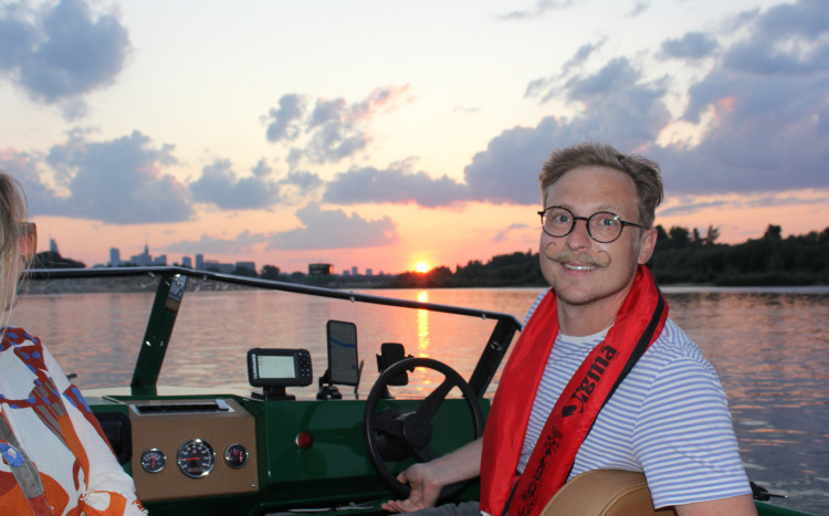 Mężczyzna z wąsem i w okularach kierujący łódką