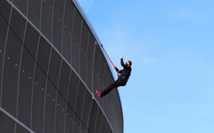 Mężczyzna skaczący ze stadionu, pokazujący za pomocą ręki symbol "OK" 