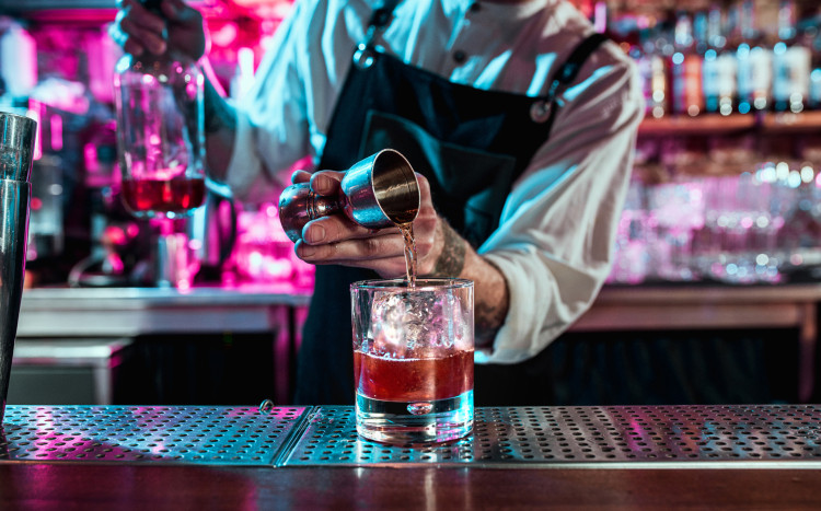 Barman wlewający do szklanki odmierzoną ilość alkoholu z miarki