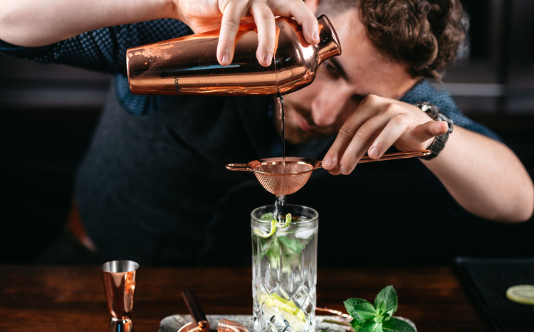 Barman przelewający gotowy drink z shakera przez sitko do szklanki