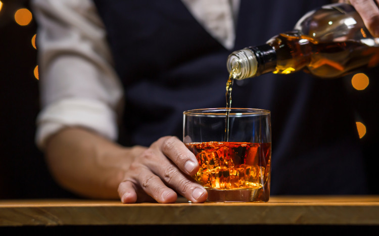 Barman wlewający whisky do szklanki z kostkami lodu z butelki z dozownikiem