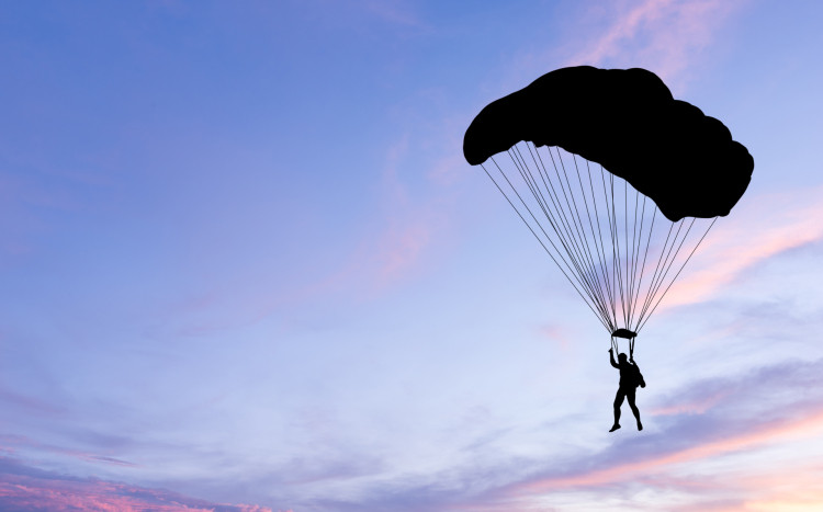 Sylwetka osoby lecącej ze spadochronem podczas zachodu na tle fioletowego nieba