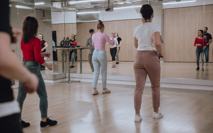 Kobiety stojące tyłem do aparatu podczas nauki tańca na sali z wielkim lustrem