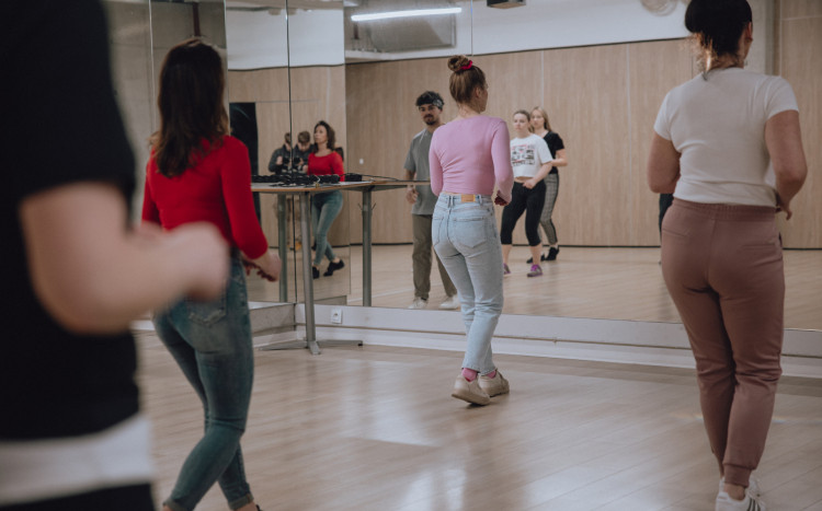 Kobiety stojące tyłem do aparatu podczas nauki tańca na sali z wielkim lustrem