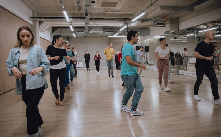 Wiele osób na jednej sali uczących się kroków tanecznych na zajęciach tańca