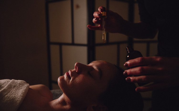 Masażystka trzymająca pipetę z olejkiem do masażu nad głową kobiety