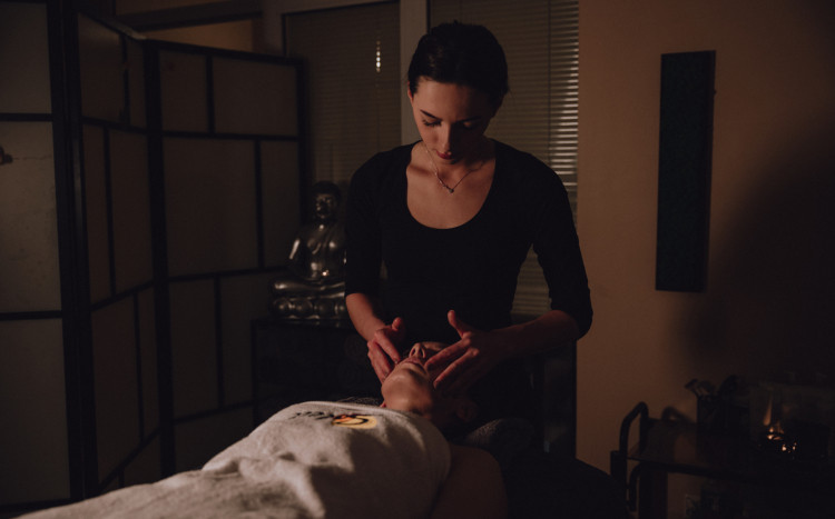 Masażystka muskająca palcami twarz kobiety podczas masażu