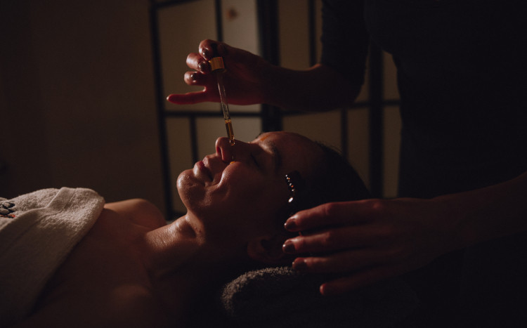 Masażystka trzymająca pipetę z olejkiem do masażu nad głową kobiety