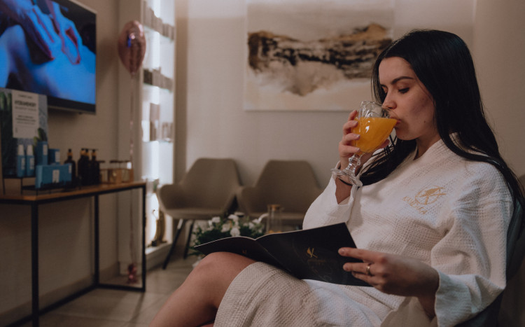 Kobieta w SPA ubrana w szlafrok popijająca pomarańczowy sok