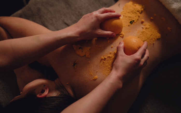 Kobieta podczas peelingu pleców dwoma połówkami pomarańczy wypełnionymi kosmetykami