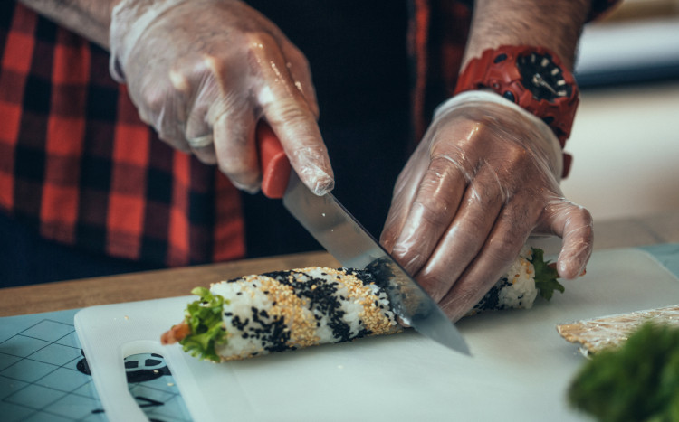 mężczyzna kroi rolkę sushi na kawałki