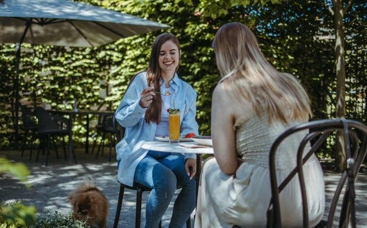 Dwie kobiety siedzące przy stoliku z jedzeniem i napojami na zewnątrz lokalu