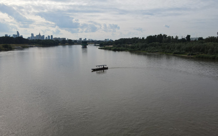 Widok z oddali na łódź płynącą po Wiśle i widok na wieżowce w Warszawie