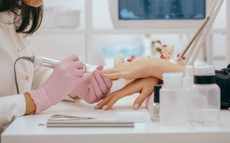 Kosmetyczka w różowych rękawiczkach podczas frezowania paznokci