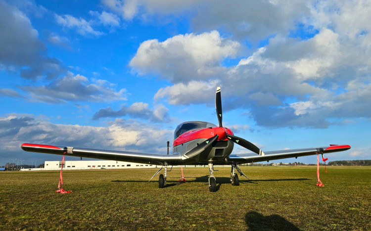 przód szaro-czerwonego samolotu stojącego na zielonej trawie na tle niebieskiego nieba