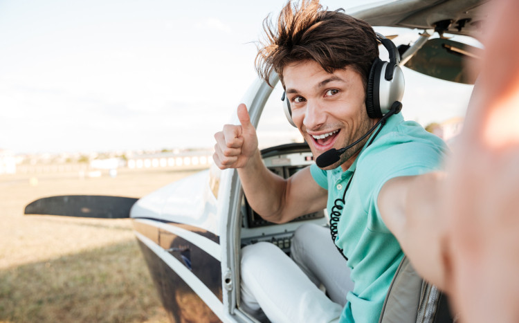 Uśmiechnięty pilot siedzący w awionetce, pokazujący gest "ok"