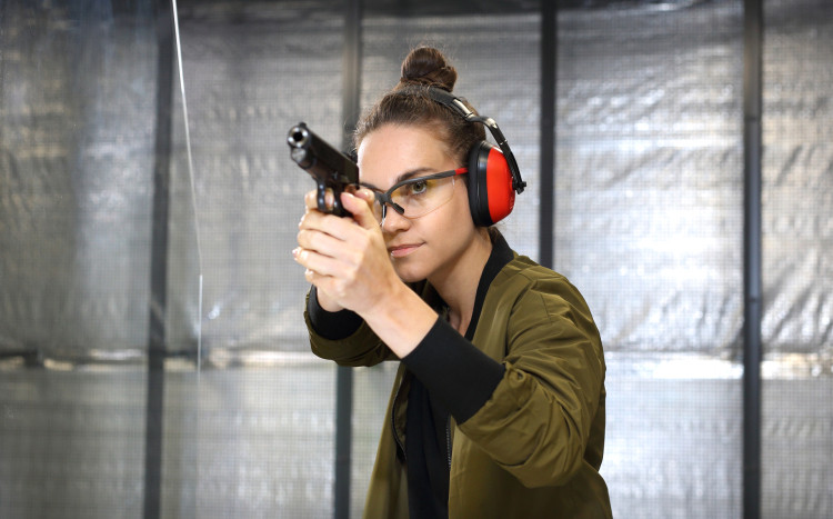 Kobieta w słuchawkach ochronnych trzyma pistolet, przygotowując się do strzału na strzelnicy