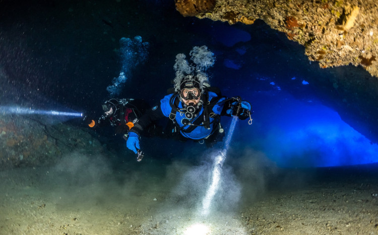 nurek z latarką płynie pod skałą