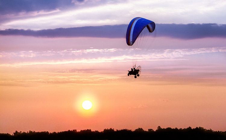 Lot motoparalotnią na tle zachodzącego słońca