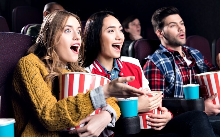 dwie przyjaciółki oglądają film w kinie i jedzą popcorn
