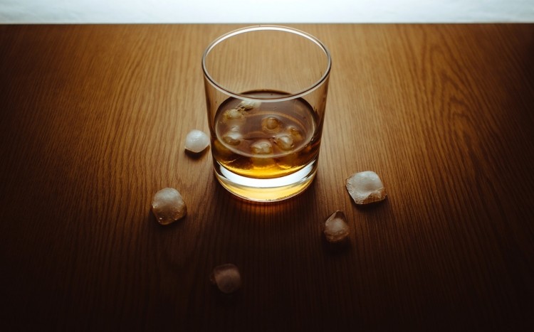 Szklanka napełniona whisky i kostki lodu leżące dookoła niej