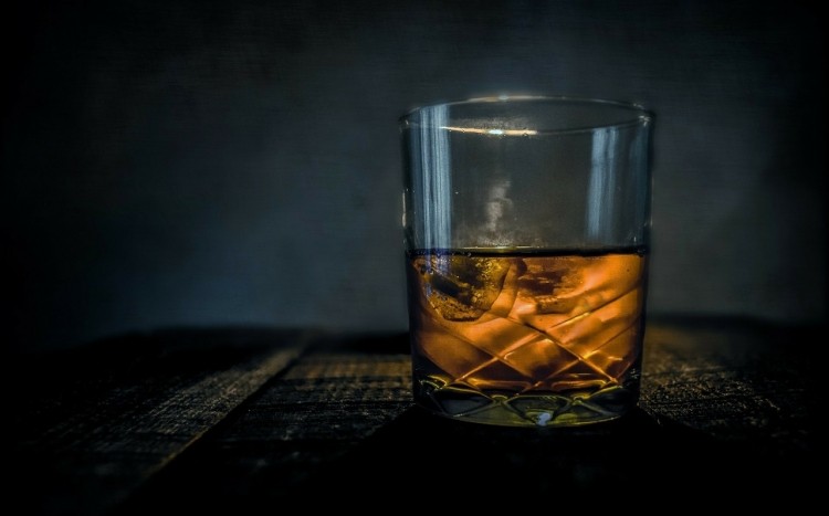 Szklanka na ciemnym tle napełniona whisky z kostkami lodu 