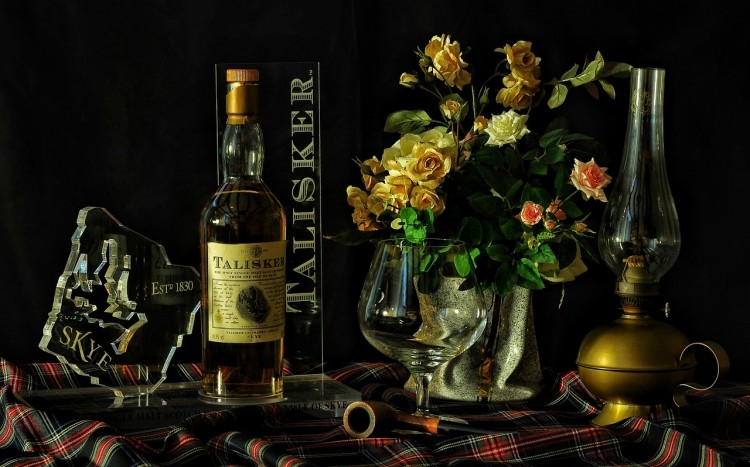 Butelka whisky Talisker Skye, a obok niej fajka, lampka i kwiaty