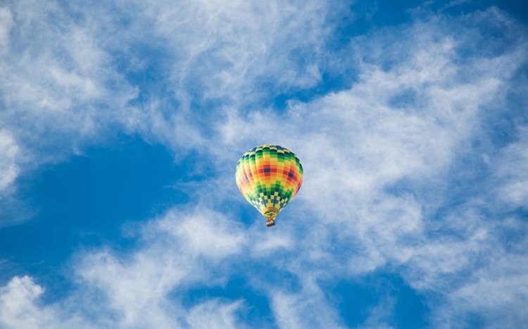Kolorowy balon w locie na tle niebieskiego nieba z delikatnymi chmurami