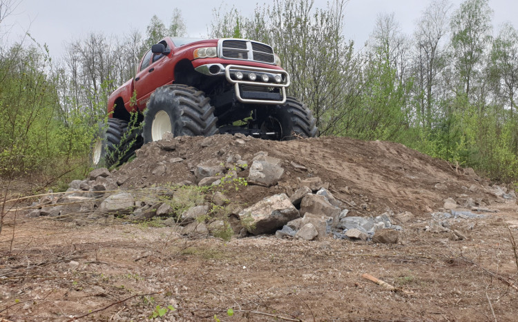 Czerwony Monster Truck wjeżdżający na niewielką górkę z ziemi