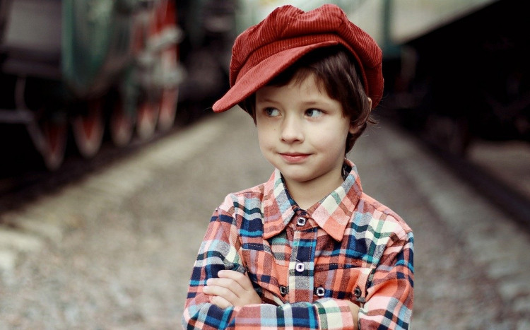 Chłopiec w kapeluszu przy lokomotywie.