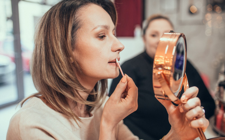 Kobieta przed lustrem maluje usta szminką