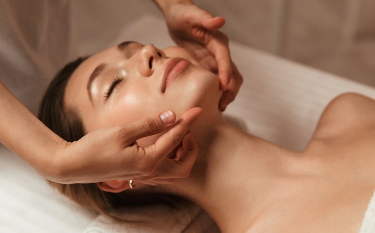 zrelaksowana kobieta z zamkniętymi oczami podczas masażu twarzy