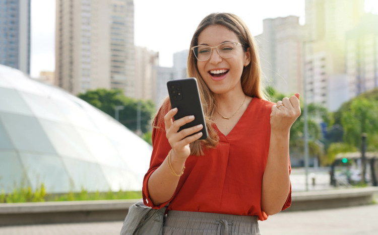 kobieta trzyma telefon w dłoni i cieszy się do ekranu