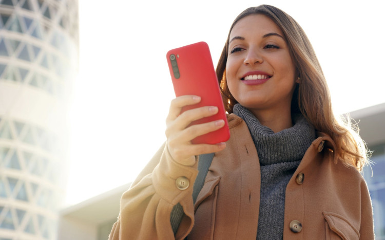 młoda kobieta trzyma w ręce telefon w czerwonej obudowie
