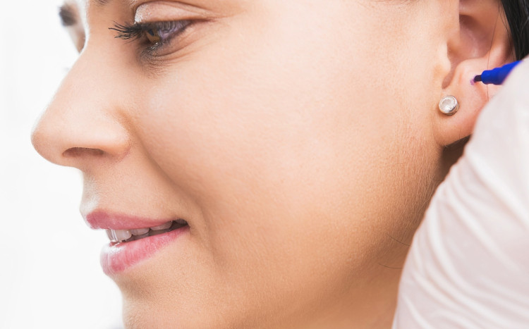 kosmetyczka zaznacza miejsce wykonania dziurki w uchu