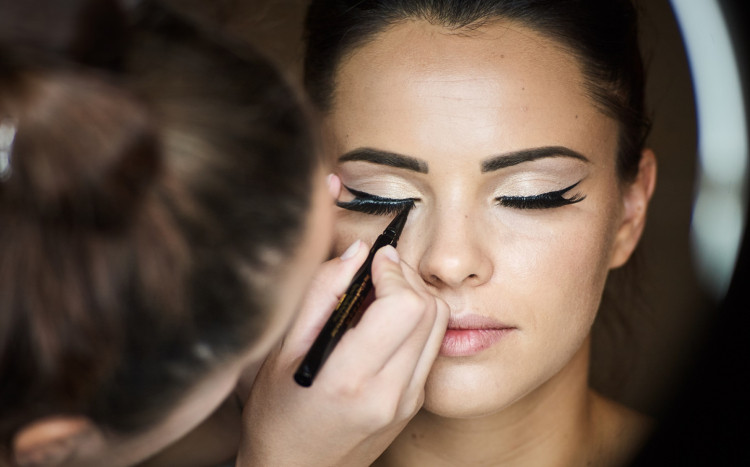 kobieta na makijażu okolicznościowym podczas malowania kresek eyelinerem