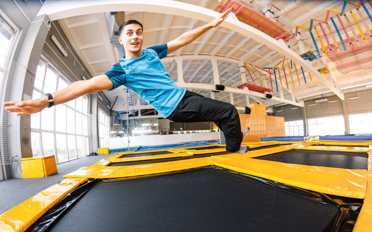 mężczyzna skacze z uniesionymi rękami na trampolinie