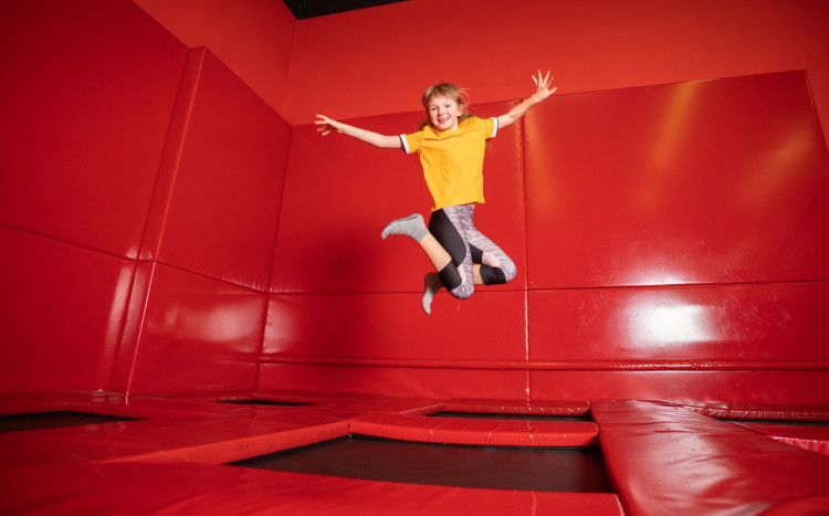 dziecko wysoko skacze na trampolinie z uniesionymi rękami