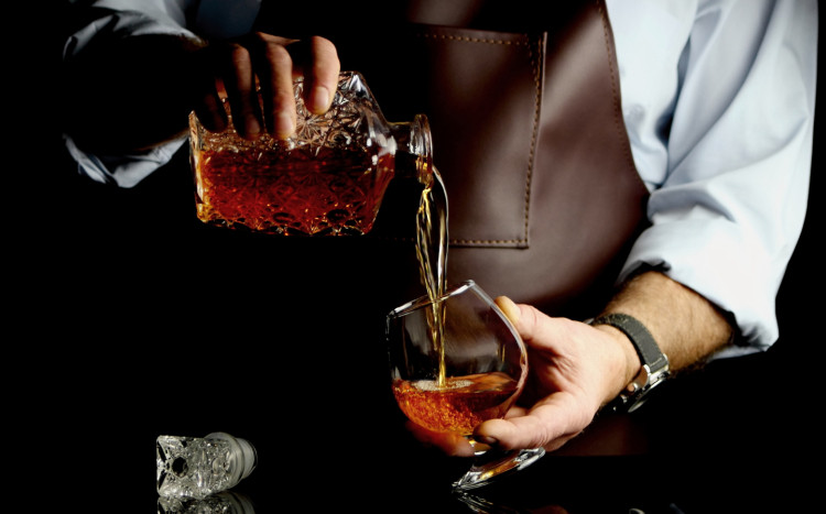 mężczyzna w brązowym fartuchu nalewa whisky do szklanki z karafki