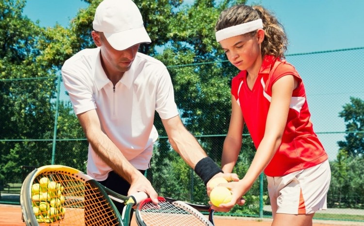 instruktor uczy dziewczynkę techniki gry w tenisa