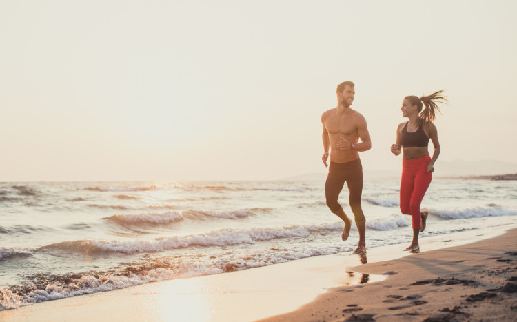 Para osób, mężczyzna i kobieta, biegają przy wschodzie słońca nad samym morzem
