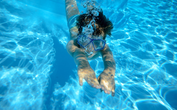 Chłopiec w okularach podwodnych nurkujący w wodzie i wypuszczający bąbelki