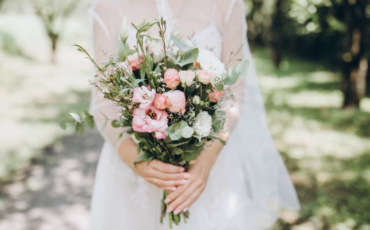 Kobieta w białej sukni trzymająca w dłoniach bukiet kwiatów