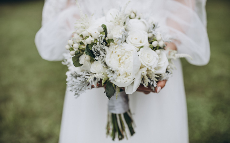 Kobieta w białej sukni trzymająca w dłoniach bukiet białych kwiatów