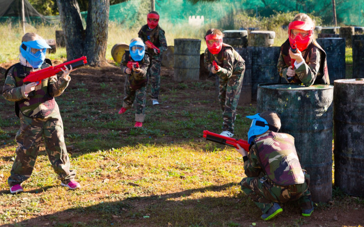 grupa dzieci w kaskach z bronią do paintballu